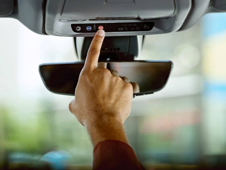 Hand pressing a button on a car's overhead console, near a rearview mirror, illustrating vehicle functionality.