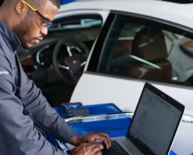 Mechanic wearing safety glasses uses a laptop for car diagnostics in a garage.