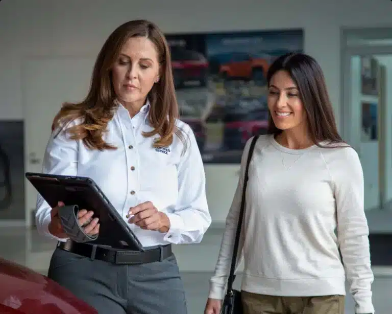 A service advisor with a tablet assists a smiling customer in a car showroom.