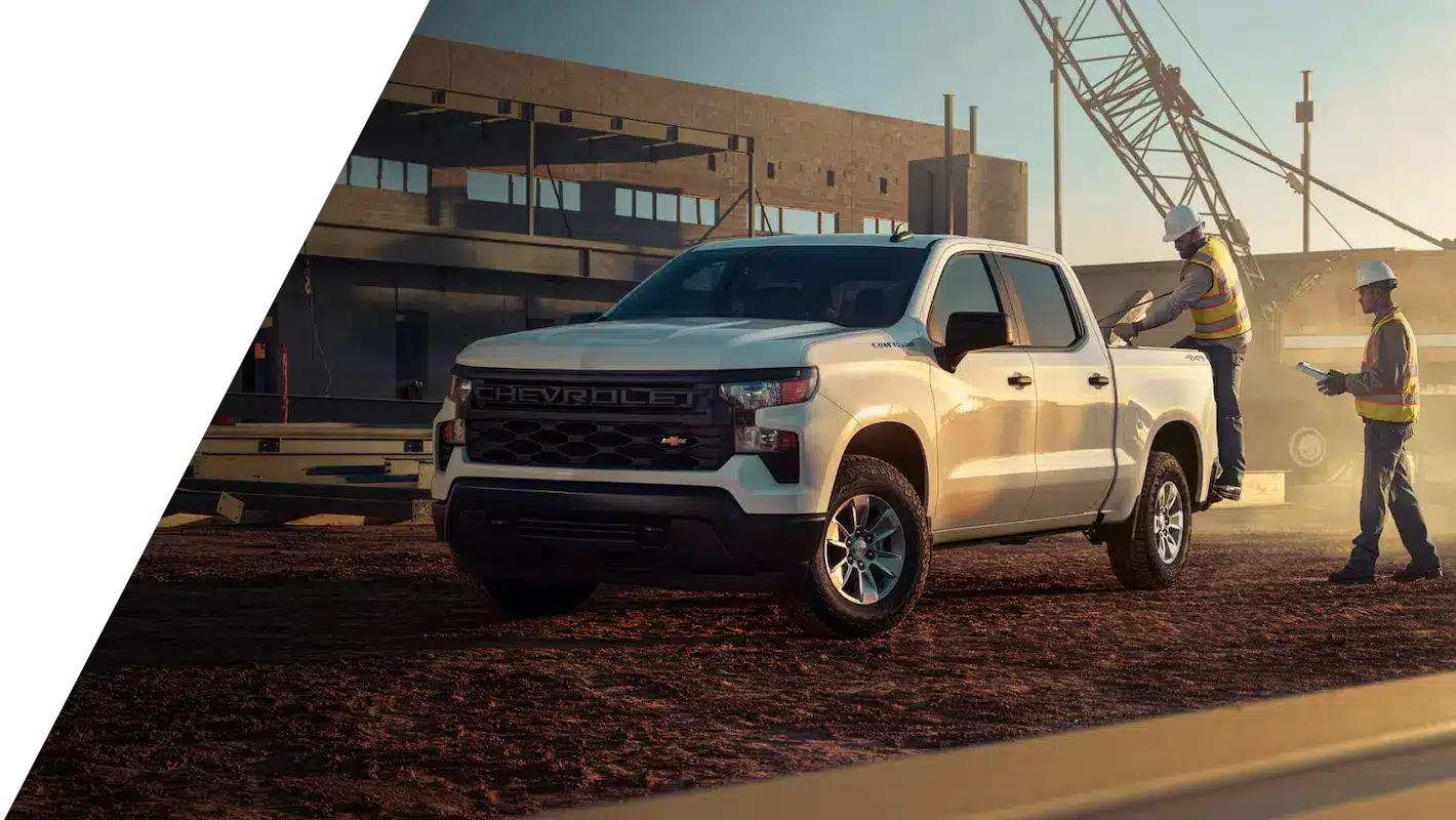 White Chevrolet pickup truck at a construction site with workers and equipment in the background.