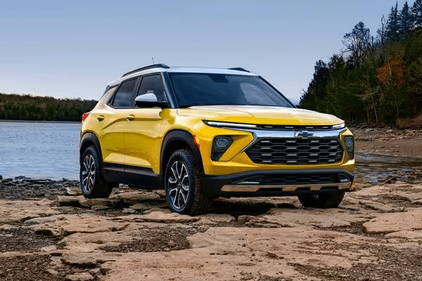 Yellow SUV parked on rocky shore near a lake, surrounded by trees, under a clear sky.