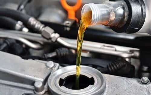 Pouring engine oil into a car engine, representing vehicle maintenance and care.