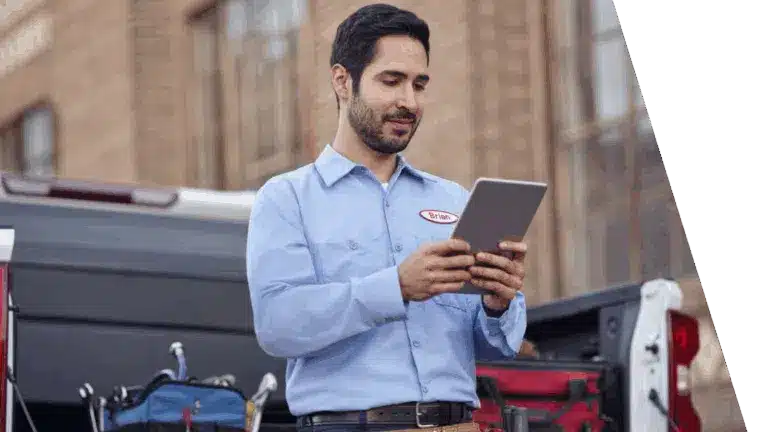 Technician in a blue shirt using a tablet near a truck, with tools visible in the background.