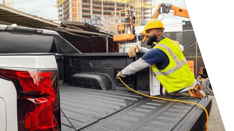 Construction worker in safety gear connects equipment in a truck bed at a building site.