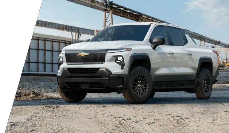 White Chevrolet pickup truck parked at an industrial site under a blue sky.