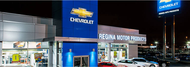 Chevrolet dealership exterior at night, showcasing Regina Motor Products signage and cars in the lot.