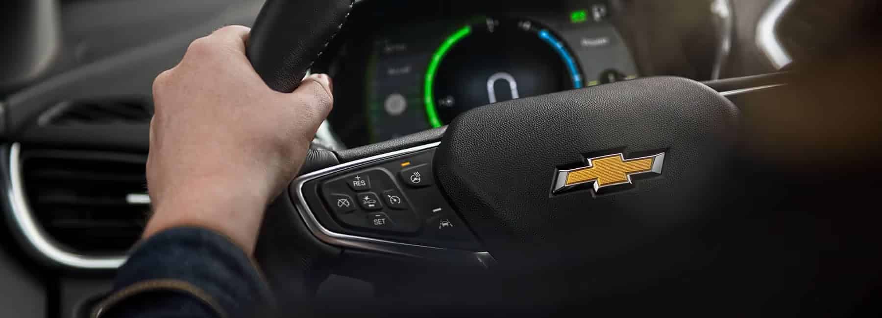Hand holding a steering wheel with Chevrolet logo, dashboard visible, showcasing car interior.