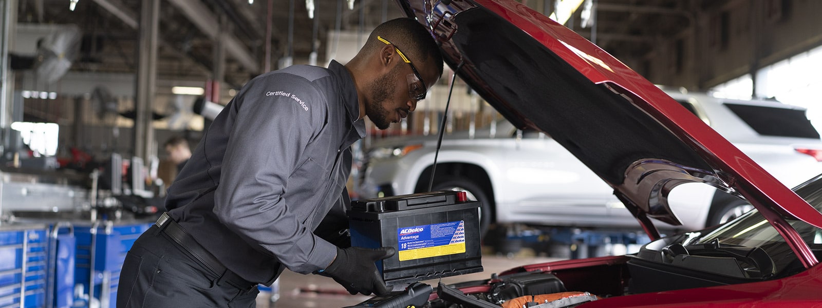 Mechanic inspecting a car's brake rotor, wearing safety glasses and gloves in a workshop.
