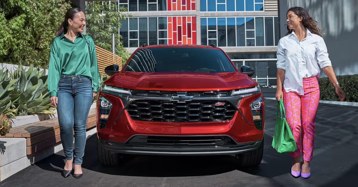 Two friends standing on either side of a red Chevrolet Trax on a city street