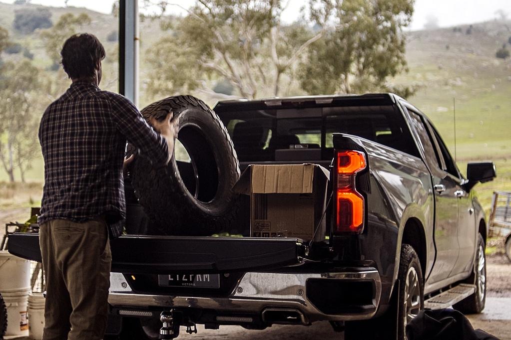 A man loading a tire into the bed of a Chevrolet Silverado on a farm